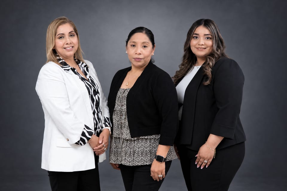 Three women stand close together in a white blazer and zebra-print scarf, a black cardigan, and a black blazer
