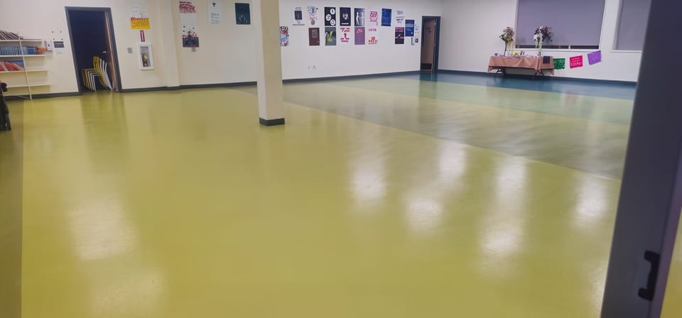 A polished olive-green school hall floor with student posters on the wall and a decorated table at the back