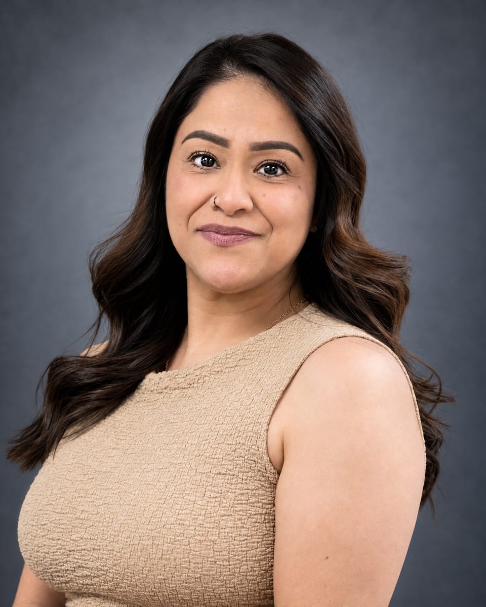Head-and-shoulders portrait of a woman with wavy dark brown hair in a beige textured sleeveless dress on a grey backdrop