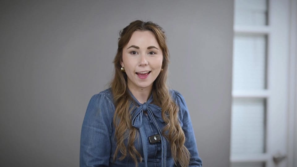 Letty Miranda smiling and speaking to camera in a denim bow blouse, a frame from the film A Long Line of Janitors